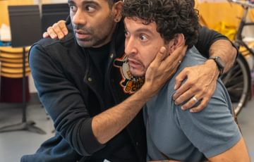 Two men sat with arms around each other, one holding a script, and both looking scared