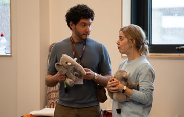 A man and a woman stood side by side looking at each other, both holding soft plush elephant teddies.