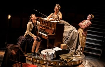 Group of women in 1940s clothes laughing around a piano