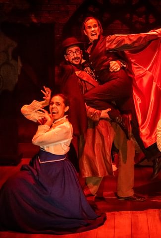 Image of 4 actors on stage with a red light, one of the actors is dressed as Dracula