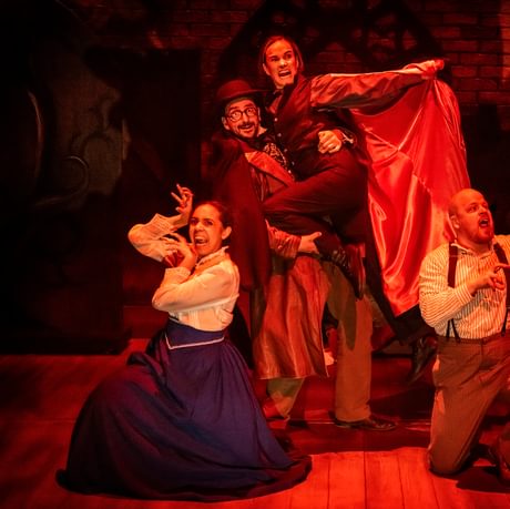 Image of 4 actors on stage with a red light, one of the actors is dressed as Dracula