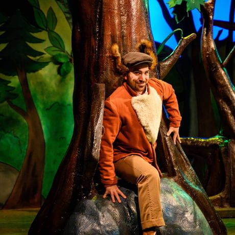 A man dress as a Fox steeping out from a tree hole