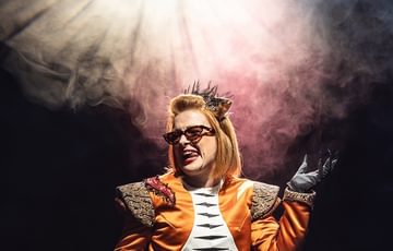 A woman posing with her tongue out with red and yellow lights in the background, and haze.
