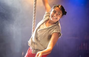 An image of a woman swinging from a rope. With blue and white lights in the background, and haze.