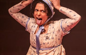 woman wearing a bonnet holding 2 sticks above her head and sticking her tongue out