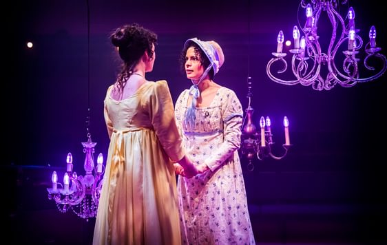 two women in regency clothing holding hands and looking intensely at each other