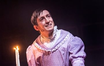 man wearing a pink dress and holding candle smiling