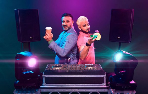 2 Asian men stood behind a DJ set. The older man has a coffee and the younger man has a cocktail.