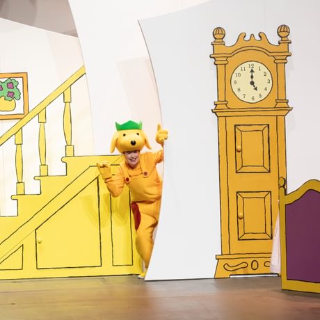 Spot the Dog wearing a green party hat standing next to a clock tower